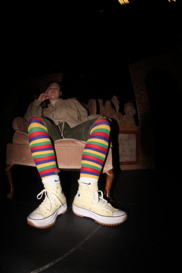 Sophomore Kate Sheley sits on a couch in her Bernardo costume in front of the set for the fall play, "The Complete Works of William Shakespeare (abridged)." The costumes of the play are based on traditional brown and green Shakespearian costumes with a twist. "It's such a wack show," Sheley said. "So putting on random colored tights is kind of the aspect of bringing a pop of color to the show."