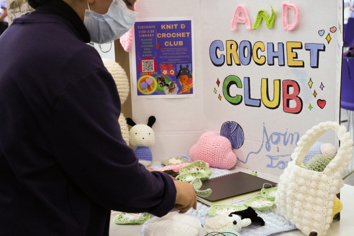 Club leader Alzhraa Mahmoud (11) arranges the poster for the Knit and Crochet club. The display included examples of projects that could be made. "Anything you can [create] with yarn, you're allowed to do in the club," Katie Weber, another of the club's four leaders, said.